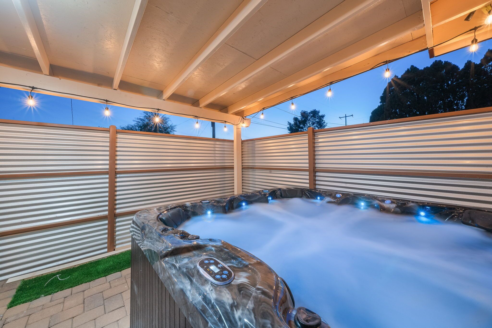 A hot tub under a covered patio with string lights, surrounded by metal railings.