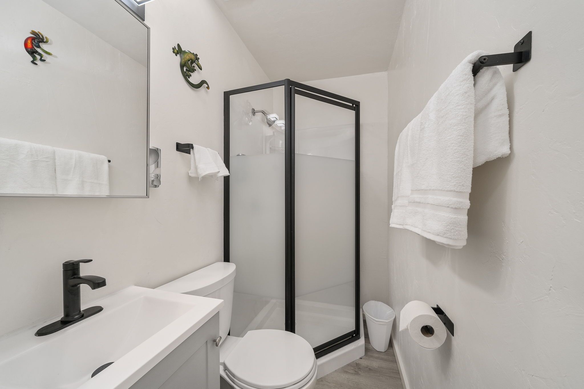 Une salle de bain avec un lavabo blanc, des toilettes et une douche fermée par des parois de verre.