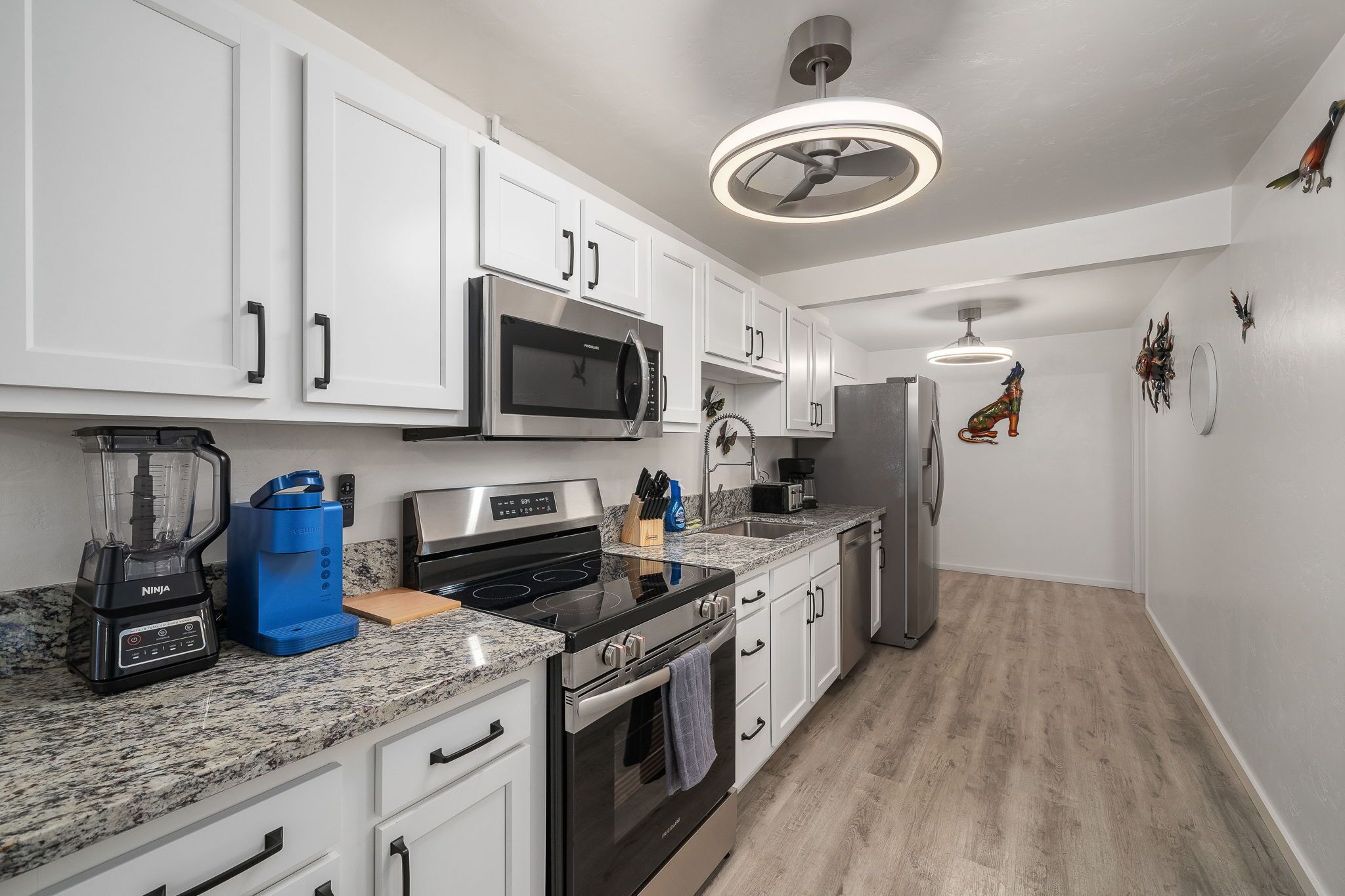 A modern kitchen with white cabinets, stainless steel appliances, a granite countertop, and a wooden floor.