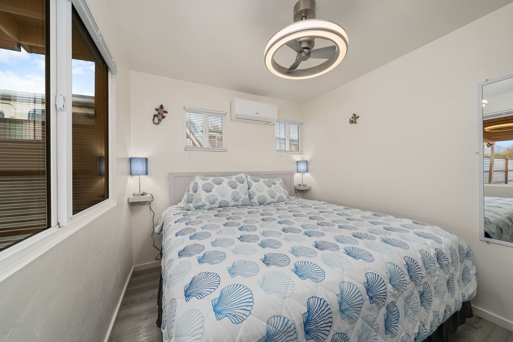 Une chambre à coucher comprenant un lit, des lampes de chevet, un ventilateur de plafond, un climatiseur et une fenêtre avec des stores.