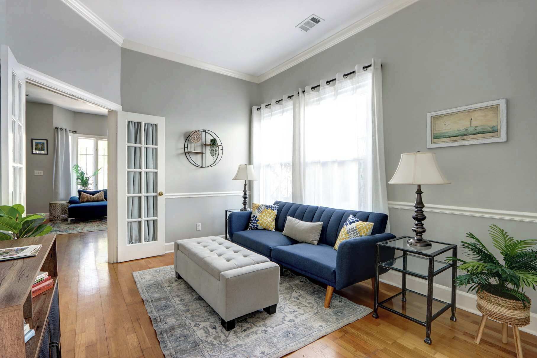 A living room with a blue sofa, a white ottoman, a glass side table, and a patterned rug.