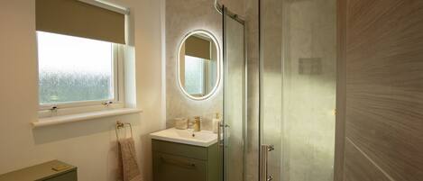 A modern bathroom with a glass-enclosed shower, a vanity with a mirror, and a window above the sink.