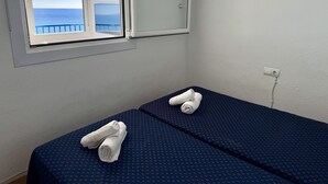 Une chambre avec deux lits, une fenêtre donnant sur la mer, une horloge murale et une prise de courant.