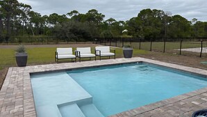 A rectangular swimming pool with a brick border, surrounded by a grassy area and a black metal fence. - New Construction, Beach Views, Private Pool, Pet-Friendly, SGI Plantation (St. George Island)