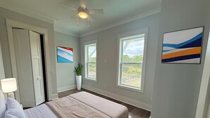 A bedroom with a bed, a ceiling fan, two windows, and a potted plant. - New Construction, Beach Views, Private Pool, Pet-Friendly, SGI Plantation (St. George Island)