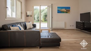 Een moderne woonkamer met een leren bank, een televisie en een schilderij van een kustlandschap.