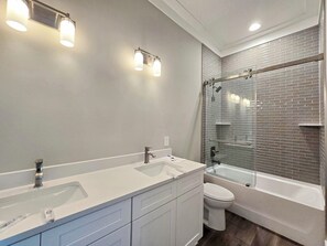 Ein modernes Badezimmer mit einem Doppelwaschtisch, einer Toilette und einer Dusche mit Glaswand und Ziegelrückwand.