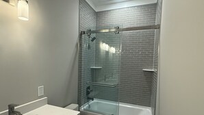 Un baño moderno con ducha de vidrio, bañera blanca y lavamanos blanco.