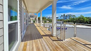 Eine Holzterrasse mit überdachtem Bereich, Geländer und Blick auf eine Wohngegend mit Häusern und Palmen.
