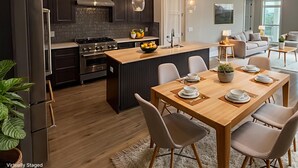 Eine moderne Küche mit dunklen Schränken, einer zentralen Kochinsel und einem Essbereich mit Holztisch und -stühlen.