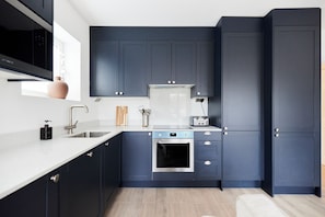 A modern kitchen with dark blue cabinets, a stainless steel oven, a microwave, and a toaster.