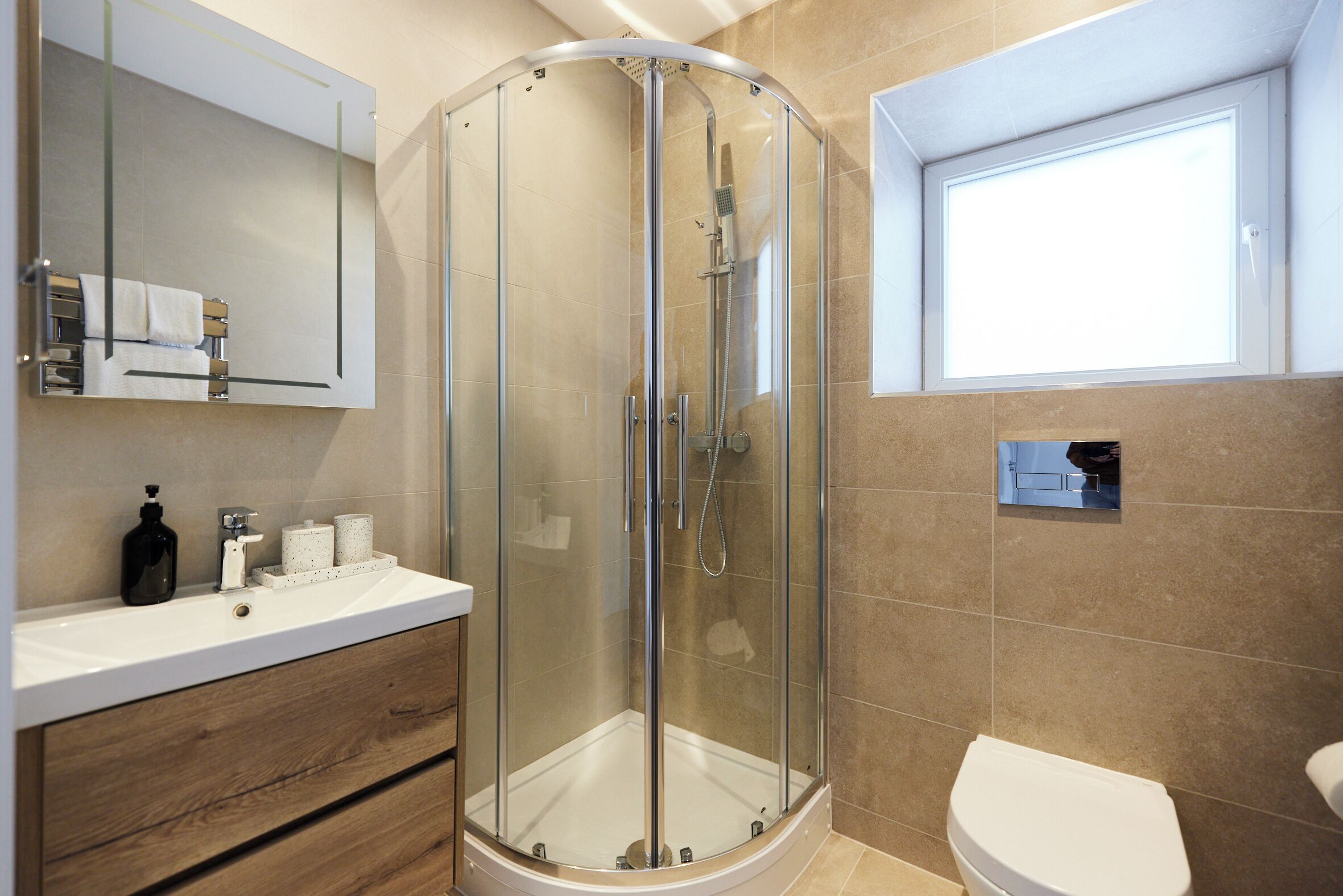 Ein modernes Badezimmer mit einer Duschkabine aus Glas, einem weißen Waschbecken mit Holzschrank und einer Toilette.