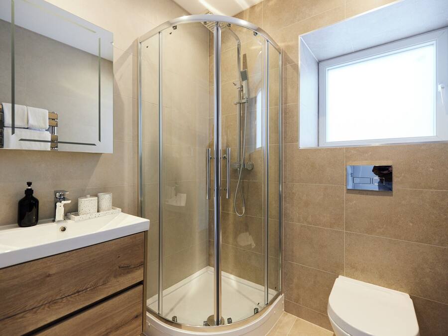 Ein modernes Badezimmer mit einer Duschkabine aus Glas, einem weißen Waschbecken mit Holzschrank und einer Toilette.