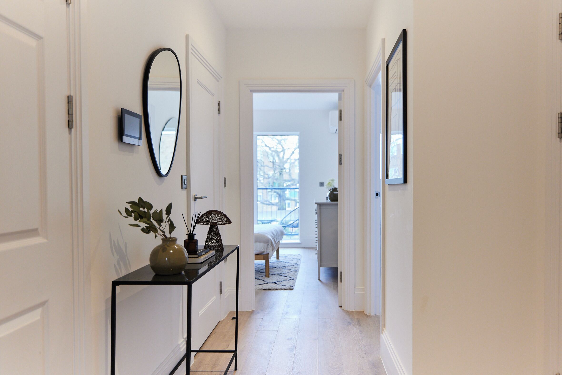 A hallway with a console table, a mirror, and a door leading to a bedroom.