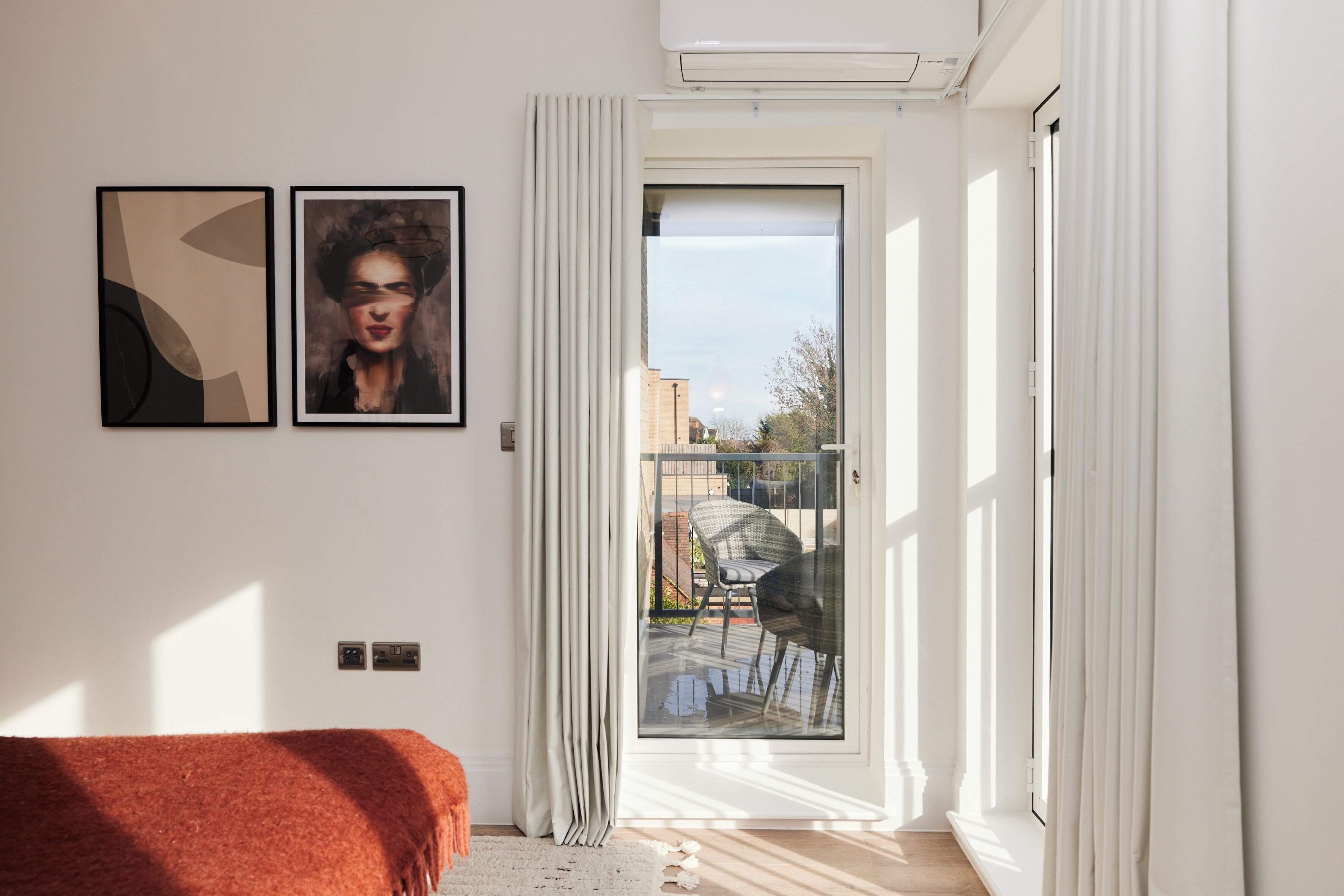 Une chambre à coucher avec un lit, une porte-fenêtre coulissante donnant sur un balcon et deux œuvres d’art encadrées accrochées au mur.