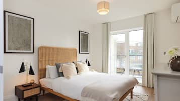 Un dormitorio con cama, mesita de noche, lámpara y vistas al exterior.