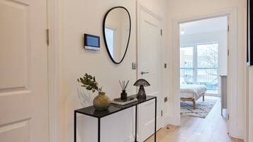 A hallway with a console table, a mirror, and a door leading to a bedroom with a bed and a view of the outside.