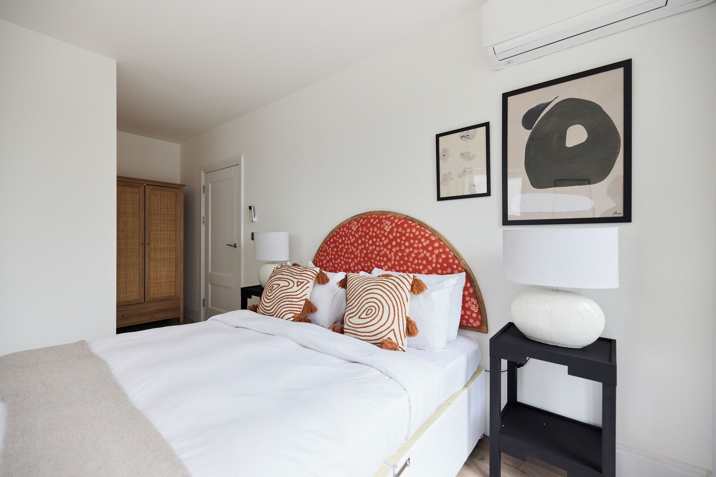 Quarto bem organizado com cama, mesa de cabeceira com abajur e uma obra de arte na parede.
