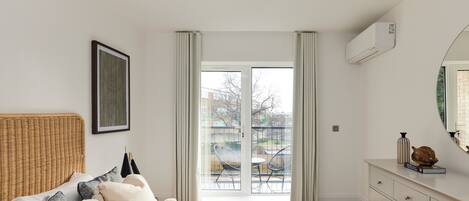 A bedroom with a bed, a dresser, a mirror, and a window with a view of the outside.