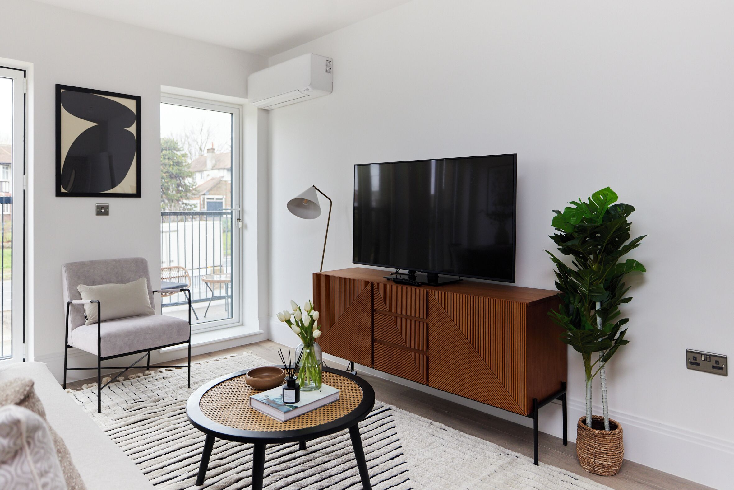Ein modernes Wohnzimmer mit einem großen Flachbildfernseher, einem bequemen Sessel, einem runden Couchtisch und einem Blumentopf.
