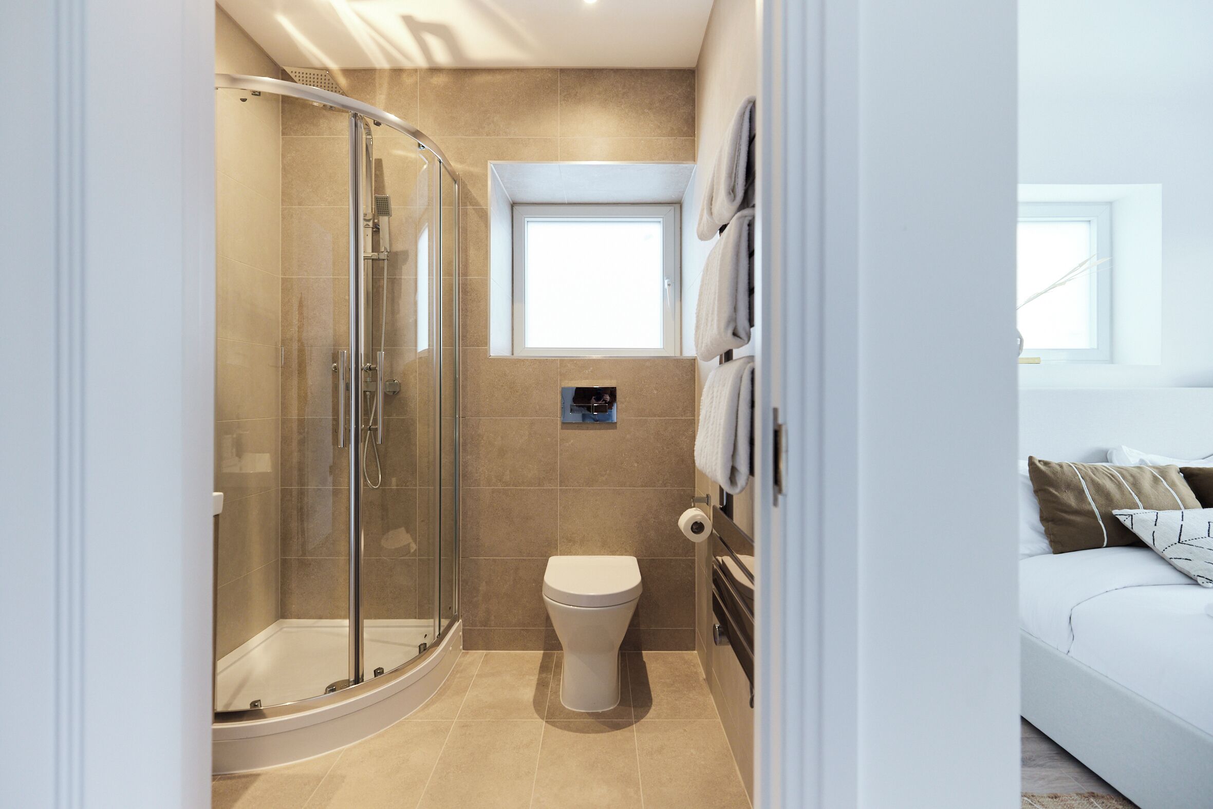A modern bathroom with a glass shower enclosure, a toilet, and a small window.