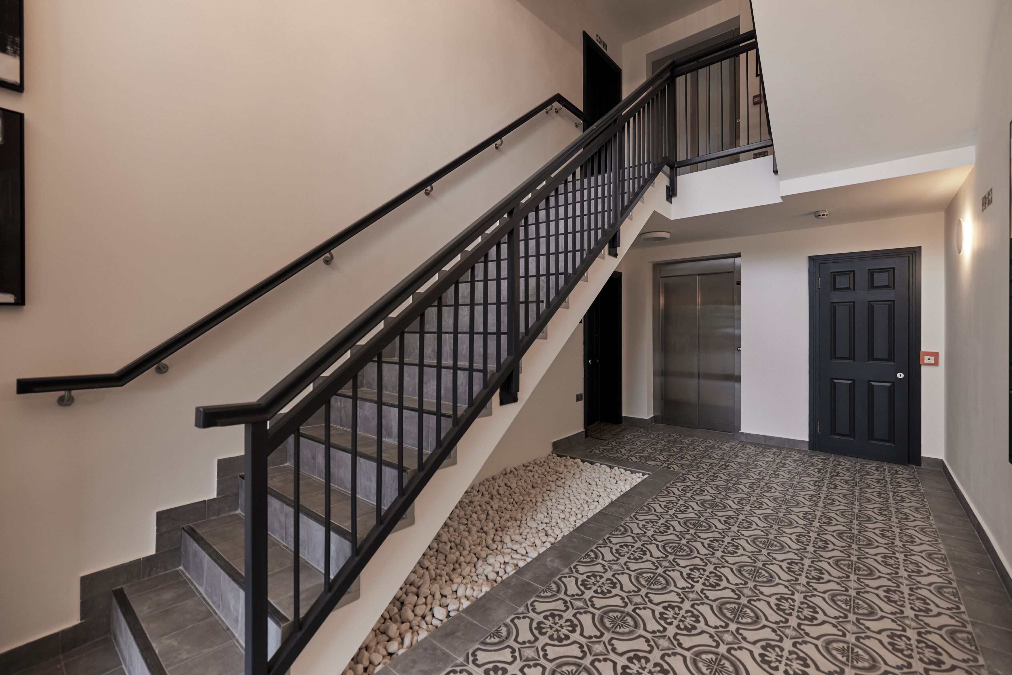 A staircase with a black railing, a patterned floor, and a door in the background.