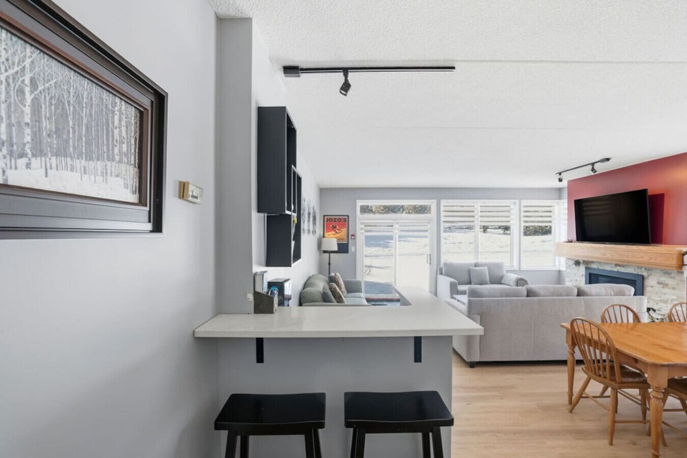 A modern kitchen with a central island, a dining area with a wooden table and chairs, and a living area with a sofa and a TV mounted on the wall.