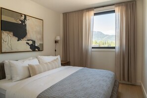 A hotel room with a bed, a painting, a nightstand, a lamp, and a window with curtains. - Monashee Meadows in Mackenzie Village (Revelstoke)