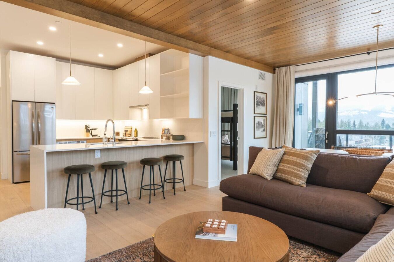 A modern kitchen with a central island, bar stools, and a large window offering a view.