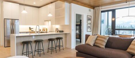 A modern kitchen with a central island, bar stools, and a large window offering a view.