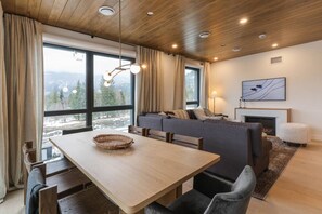 A modern living room with a wooden ceiling, a fireplace, a sofa, and a dining table with chairs. - Mountain Magic at Mackenzie Village (Revelstoke)