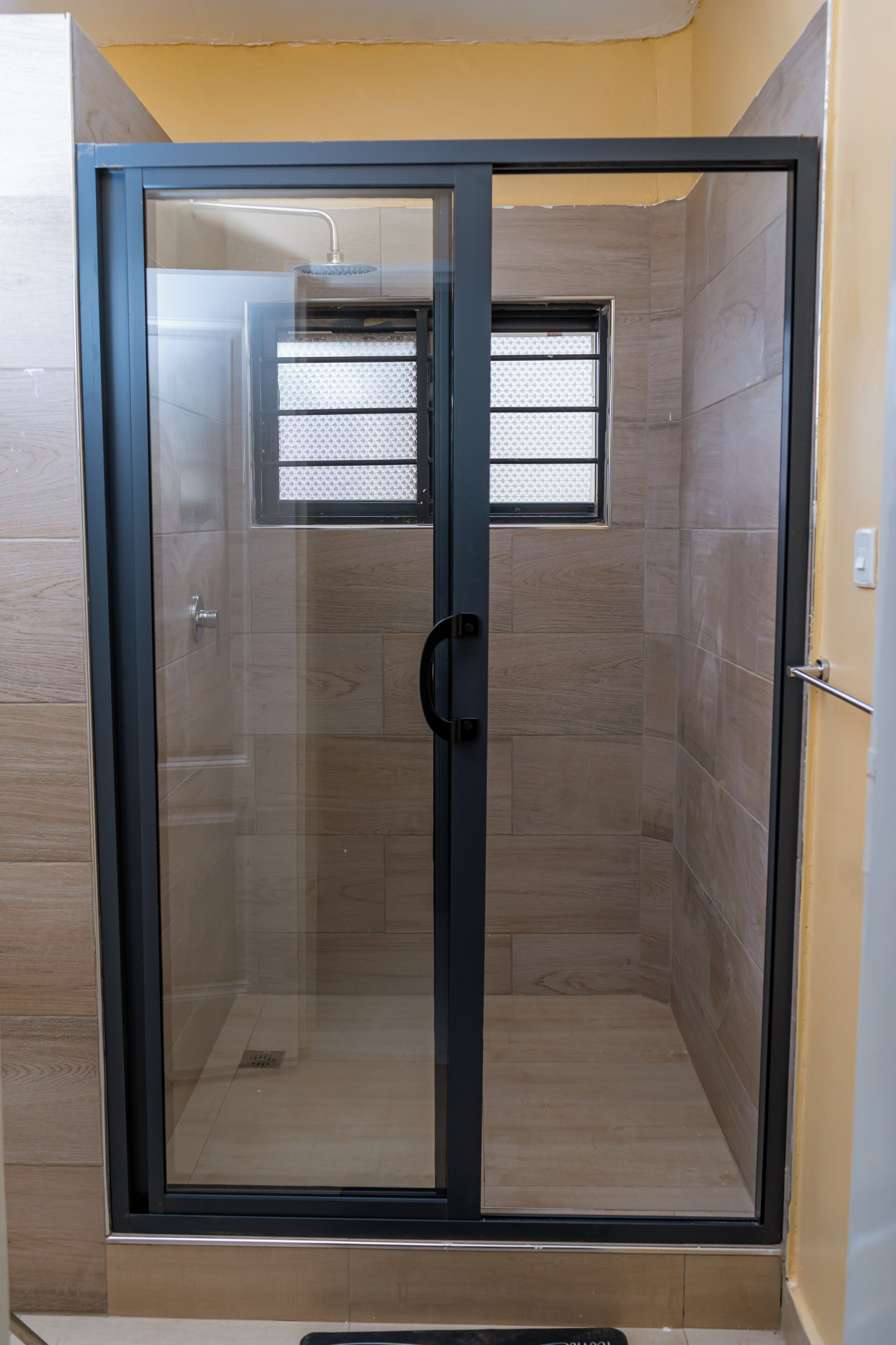 A glass-enclosed shower with a door, tiled walls, and a small window.