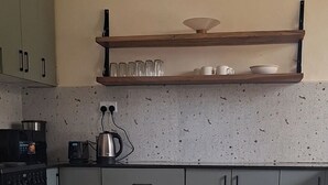 A kitchen with a stove, a kettle, and a coffee maker. There are cabinets and a countertop.