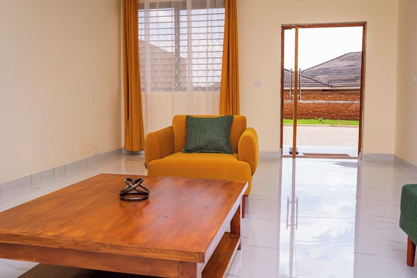 Una habitación con una mesa de madera, un sillón amarillo con un cojín verde, y vistas al aire libre a través de un ventanal.