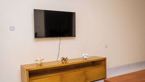 A wooden TV stand with a flat-screen TV mounted above it, a marble-tiled floor, and a wooden table to the right.