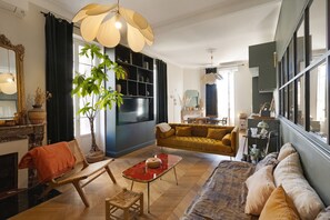 A living room with a sofa, armchair, and a dining table with a red table runner. - Charming Apartment in the Heart of Ajaccio (Ajaccio)