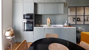 A modern kitchen with grey cabinets, a black countertop, and a dining area with wicker chairs. - Charming Apartment in the Heart of Ajaccio (Ajaccio)