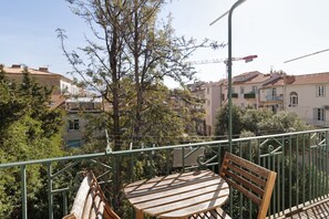 Een balkon met een houten tafel en stoelen, omringd door een metalen hekwerk.
