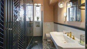 A modern bathroom with a black and white herringbone floor, a white sink with gold fixtures, and a glass shower enclosure. - Charming Apartment in the Heart of Ajaccio (Ajaccio)