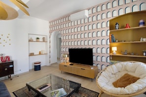 Una sala moderna con una televisión de pantalla plana, una mesa de centro de vidrio, una silla de mimbre y una pared con diseño.
