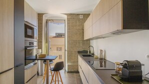Een moderne keuken met een inbouwoven, een koffiezetapparaat en een klein eethoekje met krukken.