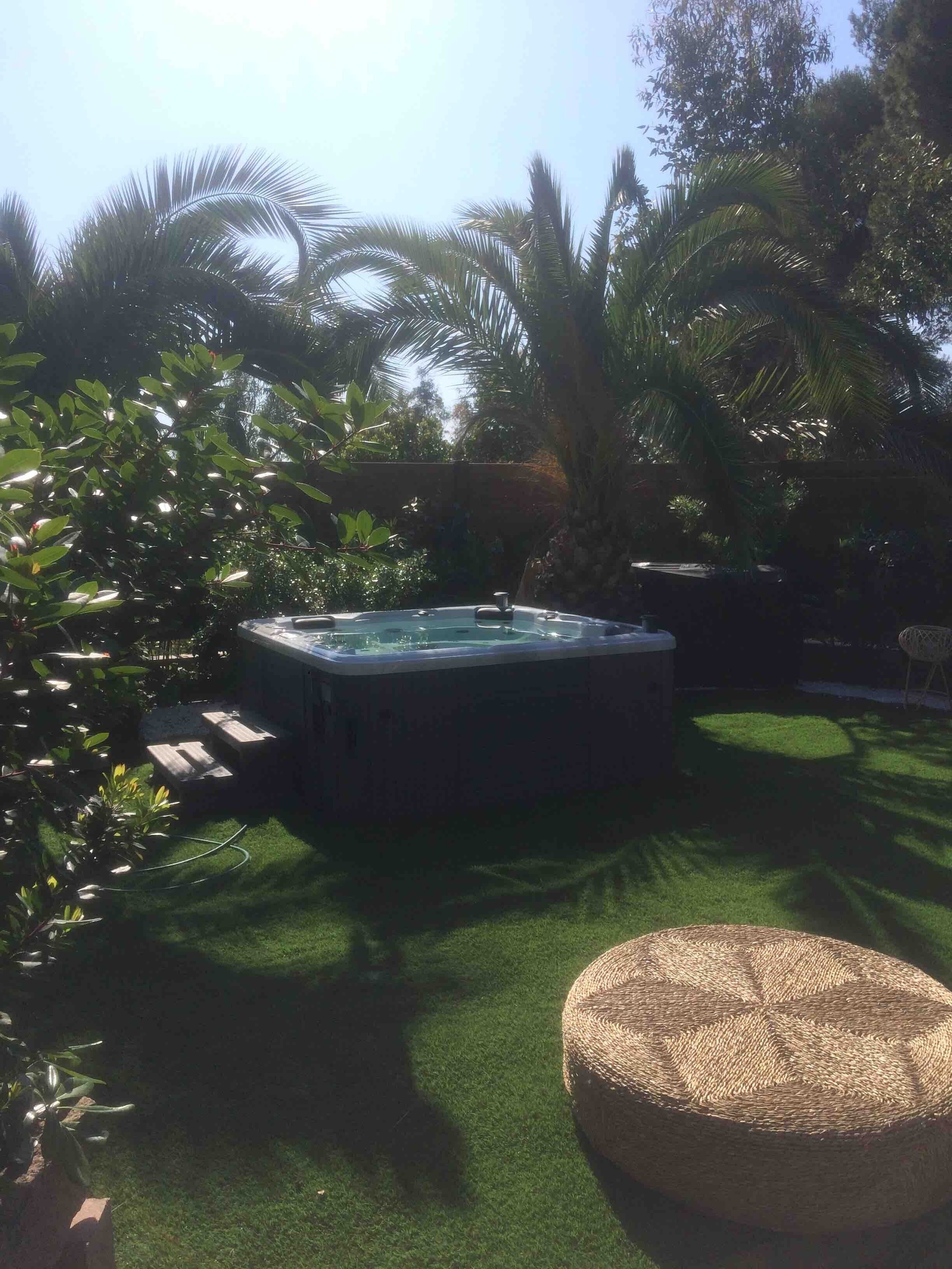 Un jacuzzi rodeado de exuberante follaje y un otomano tejido.