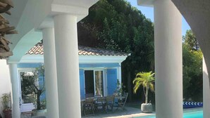 A covered outdoor area with a pool, wooden deck, and a small building with blue doors. - Charming Waterfront Villa in Pietrosella, Corsica (Pietrosella)
