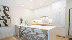 Eine moderne Küche mit weißen Schränken, einer zentralen Kochinsel mit Barhocker und einem großen, abstrakten Gemälde an der Wand.