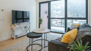 Ein modernes Wohnzimmer mit großem Fenster, einem Flachbildfernseher, einer Couch und einem kleinen Tisch.