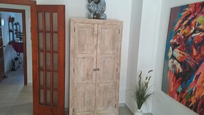 A wooden cabinet with a decorative sculpture on top, a potted plant, and a colorful abstract painting on the wall. - ALBIR, apartment for 4 pers., ground floor with garden, 100m to the beach, super pool, air conditioning (L’Alfàs del Pi)