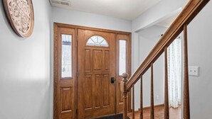 Une porte d’entrée en bois avec un panneau de verre, un paillasson et un escalier en bois muni d’une main courante.