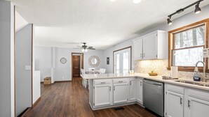 Une cuisine moderne avec des meubles blancs, un lave-vaisselle et une fenêtre donnant sur les arbres.