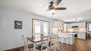 Une cuisine moderne avec des meubles blancs, un îlot central et un ventilateur de plafond.