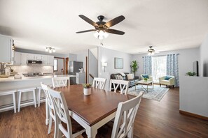 Een moderne keuken met witte kasten, een houten eettafel en een plafondventilator.